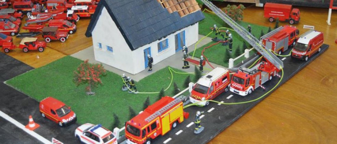 Maquette d'une maison et de véhicules de pompiers tout autour.