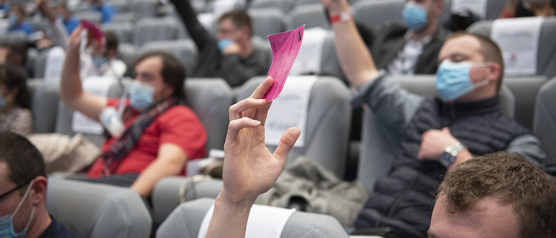 Des congressistes assis dans des fauteuils qui votent en levant des petits cartons.