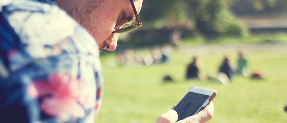 81% des agriculteurs utiliseraient internet pour leur travail au moins une fois par jour. Jeune homme regardant son téléphone portable, dans un parc.