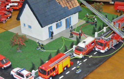 Maquette d'une maison et de véhicules de pompiers tout autour.