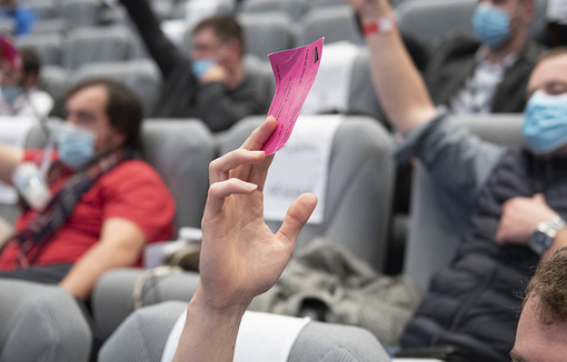 Des congressistes assis dans des fauteuils qui votent en levant des petits cartons.